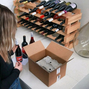 A person opening a box of wine with a winerack in the background.