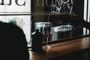 A glass of red wine being poured on a wooden bar.